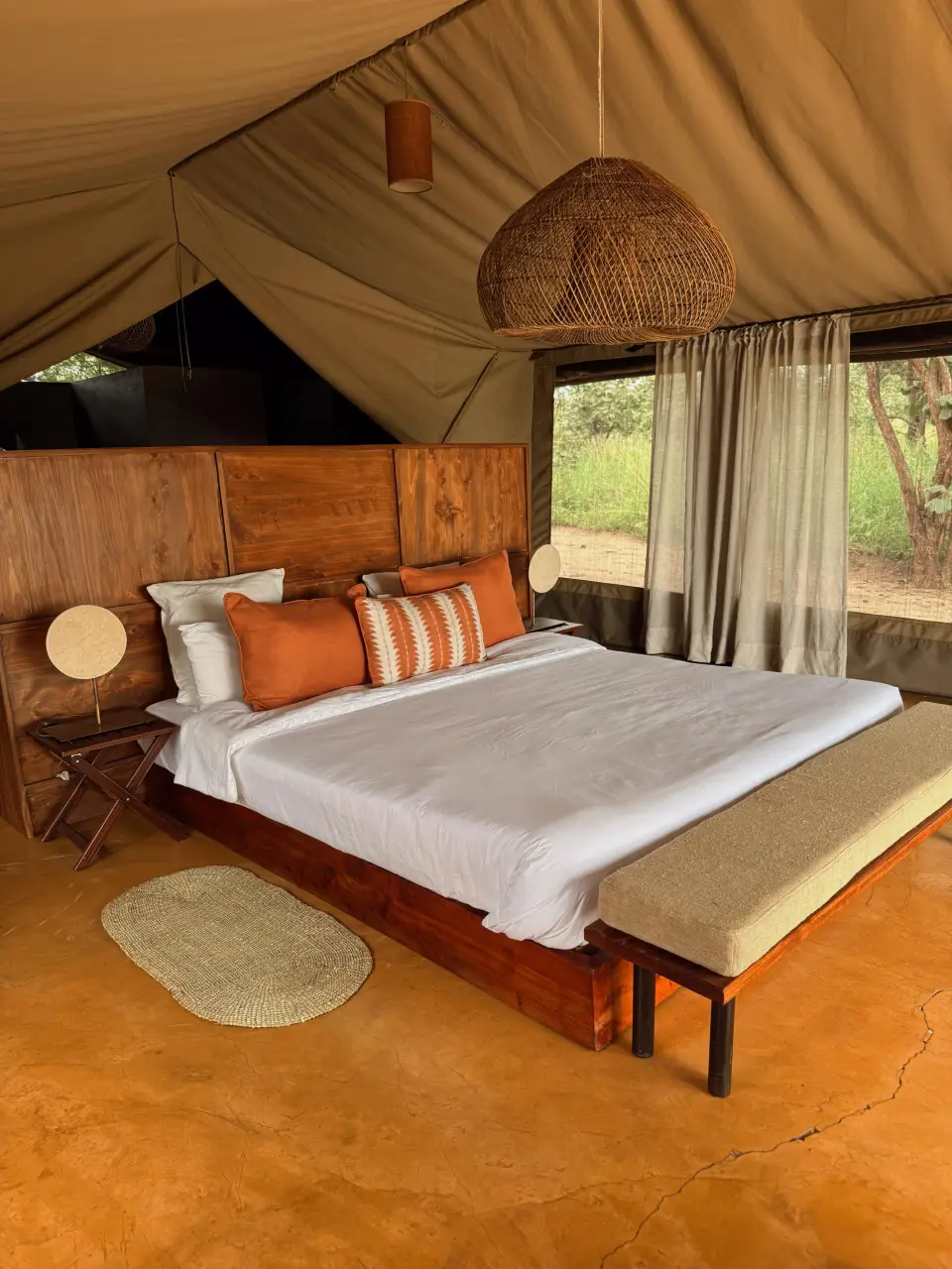 A bed with orange cushions beneath a canvas roof and a woven pendant lamp