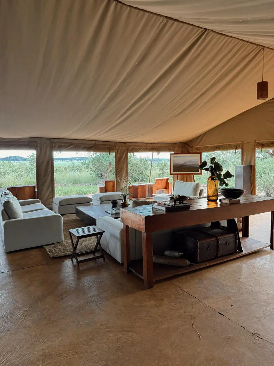 A lounge corner inside a tent, with sofas and a writing desk facing the bush