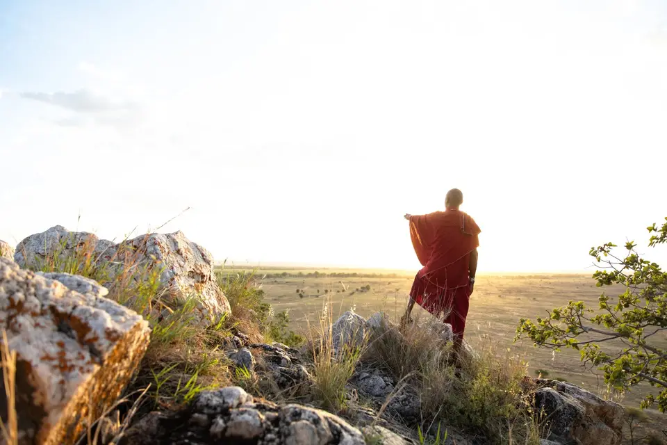 A Maasai man stands on rocks looking out over the plains
