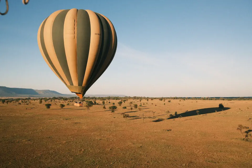 A striped hot air balloon lifting off over golden grassland in early light