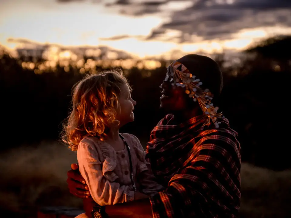 A Maasai woman and a young guest smiling at each other at sunset