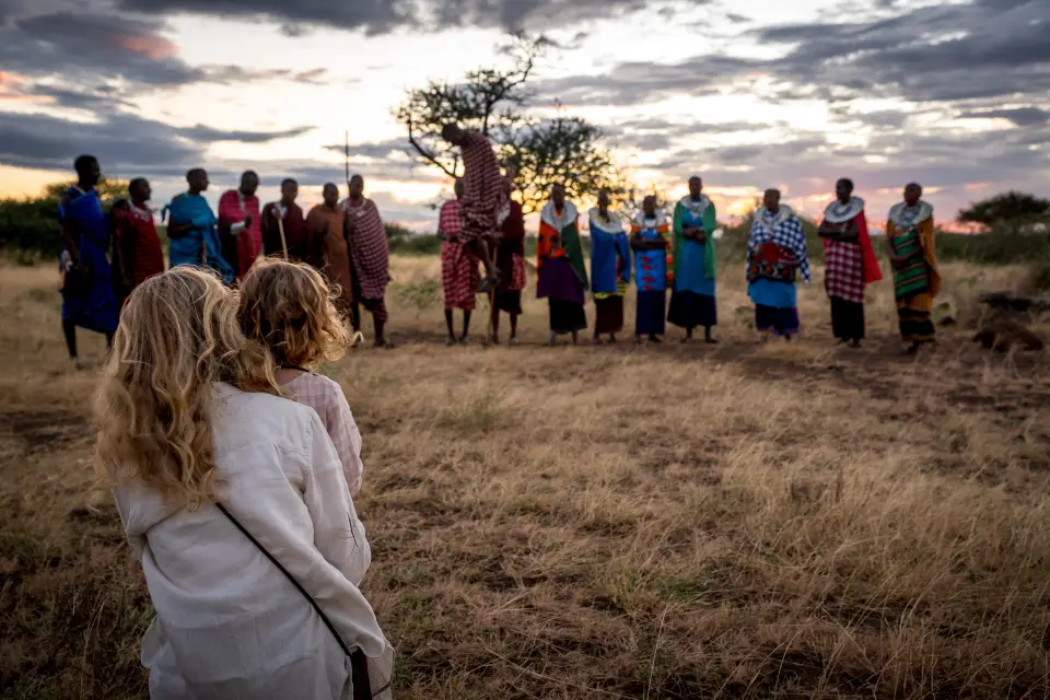 Guests watching a line of Maasai men and women singing in a clearing at dusk