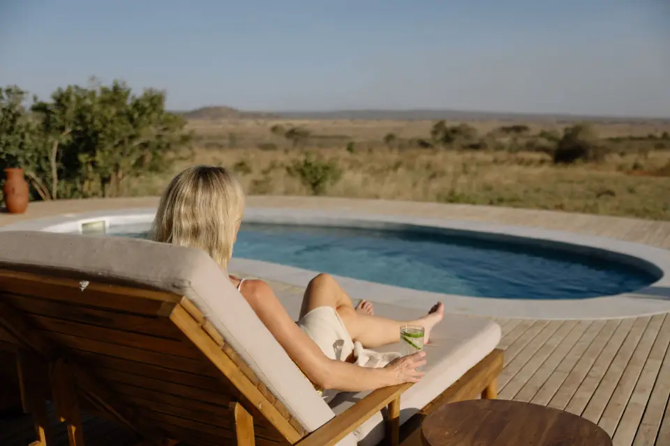 A guest reading on a lounger beside the lodge pool, the plains beyond