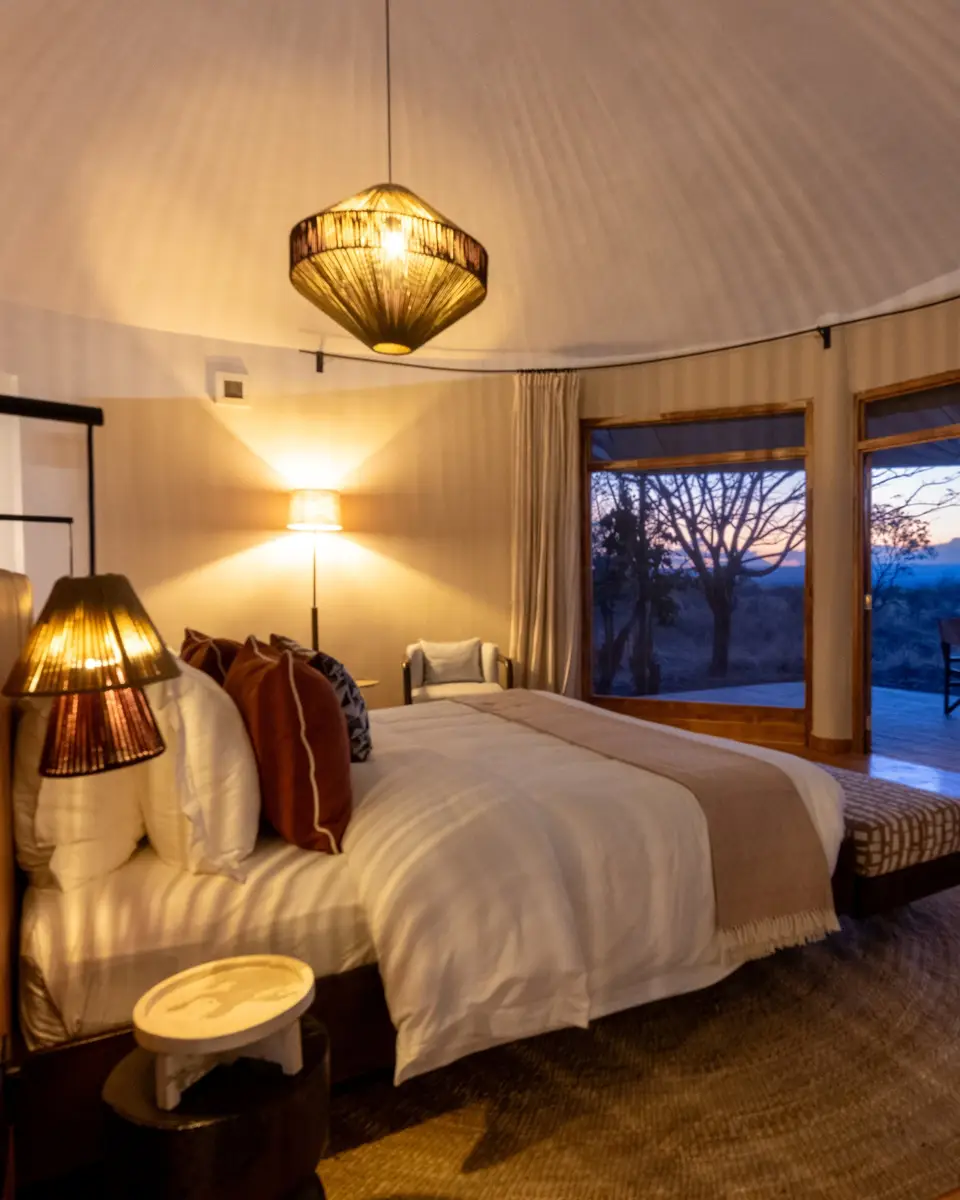Inside a banda, the bed looks out through wide windows to the bush