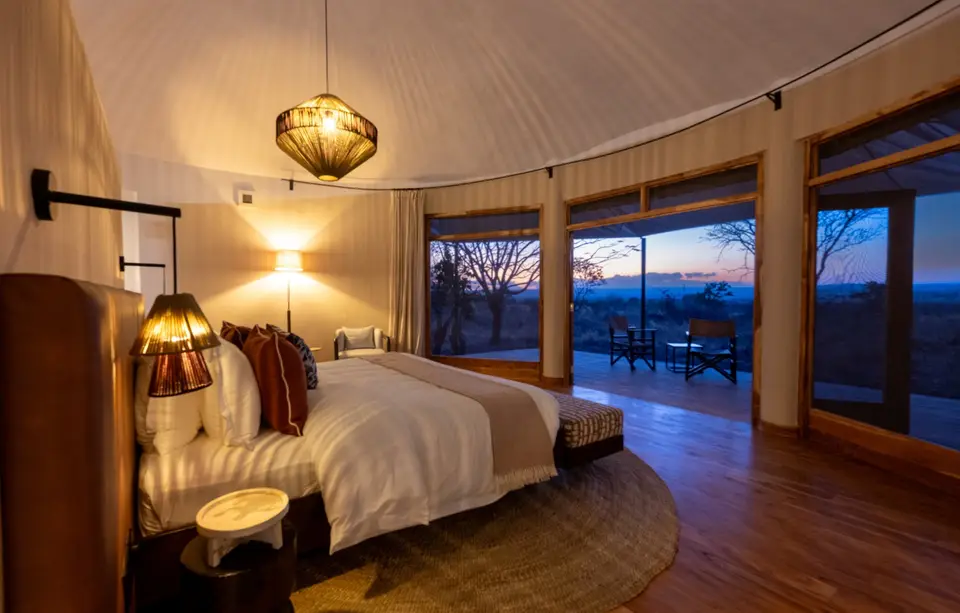 Inside a banda, the bed looks out through wide windows to the bush